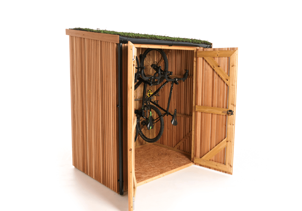 A vertical bike shed crafted from Scottish Larch cladding wood, featuring a green grass roof. Its double doors are open, revealing bicycles stored vertically on a wall mount inside.